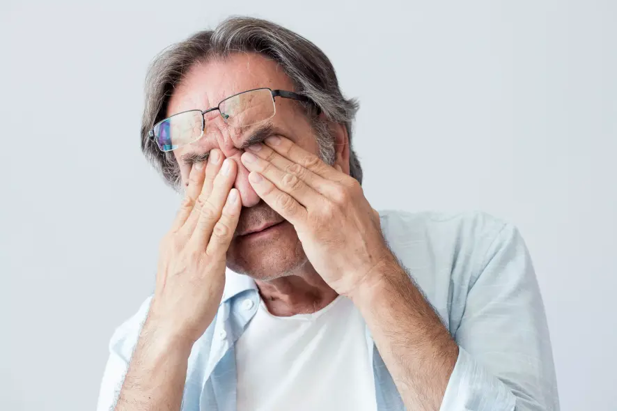 Alterer Mann reibt sich wegen Augenschmerzen die Augenpartie