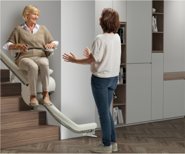 aeltere-dame-faehrt-treppenlift-in-empfangnahme-tochter Exemplarische Darstellung einer Kundin bei der Nutzung des Treppenstuhls im Gespräch | TK Home Solutions