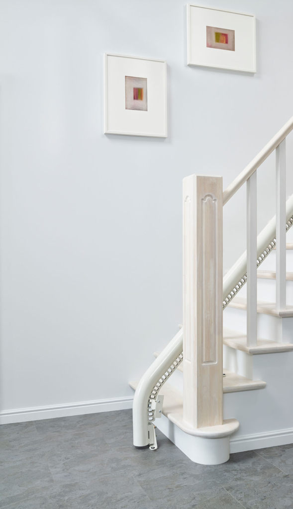 schienenlauf-am-gelaender-mit-bodenende Gerade weiße Treppenliftschiene fixiert am Boden vor erster Stufe der weißen Treppe zur Geländeseite hin | TK Home Solutions