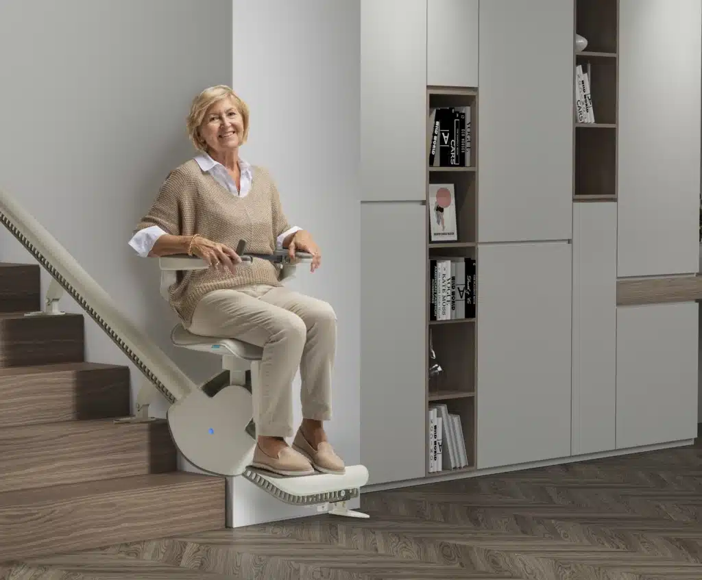 aeltere-dame-faehrt-mit-treppenlift2 Eine ältere Dame fährt mit dem Treppenlift nach unten und schaut dabei lächelnd in die Kamera | TK Home Solutions