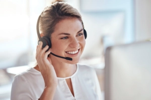 Eine Frau trägt ein Headset bei einem Videoanruf und sitzt vor einem Bildschirm. Die Kamera ist von vorne auf die Frau gerichtet | TK Home Solutions