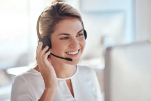 Eine Frau trägt ein Headset bei einem Videoanruf und sitzt vor einem Bildschirm. Die Kamera ist von vorne auf die Frau gerichtet | TK Home Solutions