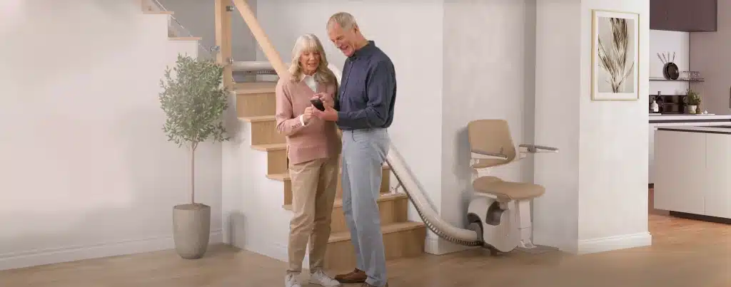Header_Bild-aelteres-paar-vor-treppe-mit-lift Älteres Paar steht vor Treppenlift und recherchiert auf einem Handy | TK Home Solutions
