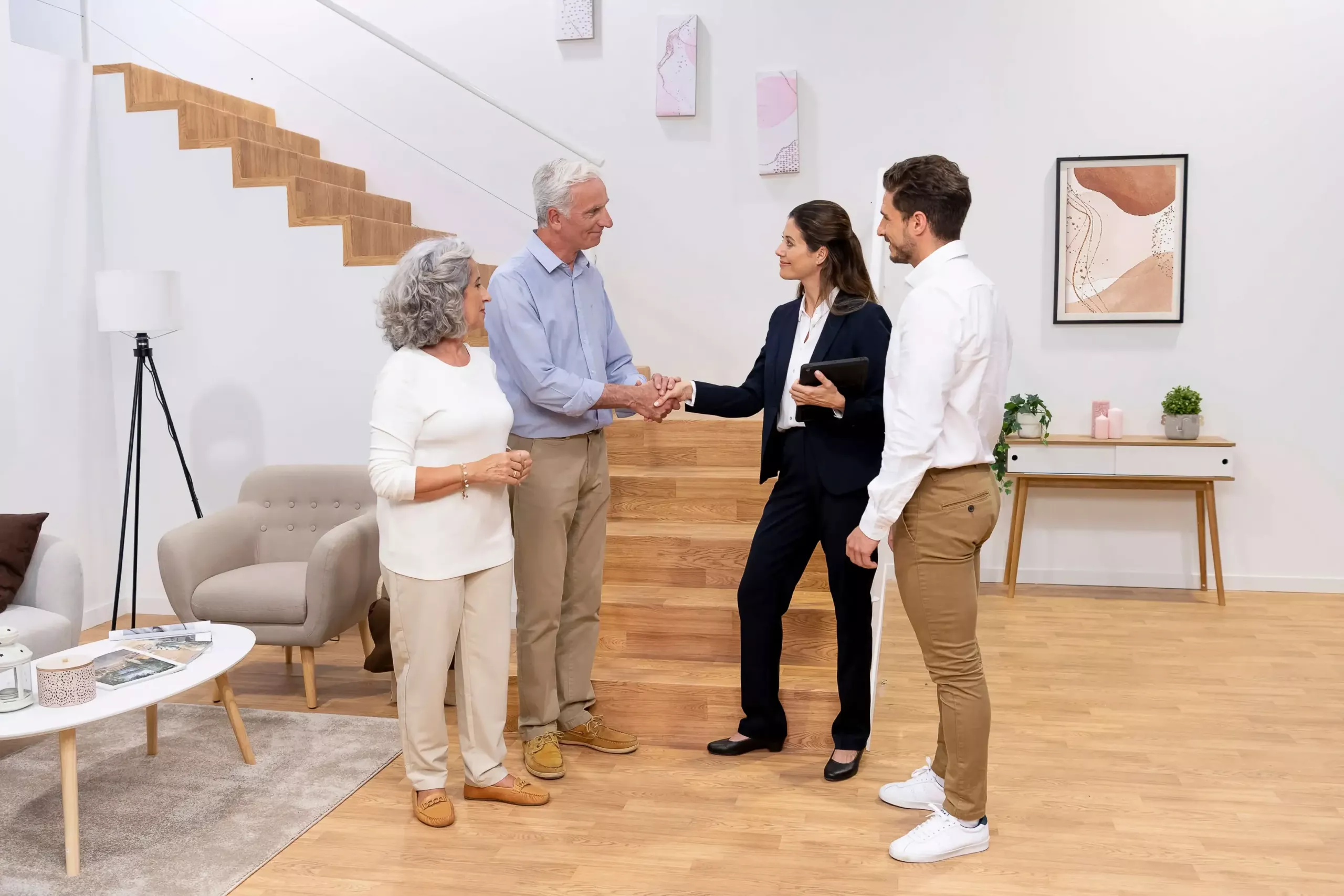 Eine Beraterin besiegelt einen Vertrag über einen Treppenlift mit einem Handschlag mit dem Mann eines älteren Paares | TK Home Solutions