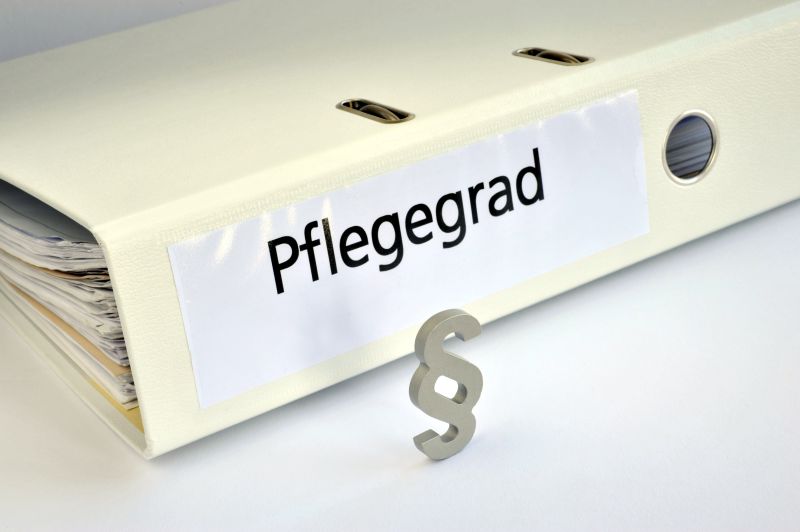 Pflegegrad, Pflegegrade, Paragraph, Recht, Gesetz, Ordner, Pflegenotstand, symbolisch, Altenpflege, Pflegeheim, Pflegeberuf, Pflegedienst, Pflegestufen, Sozialstaat, Behinderung Ein Cremefarbener Aktenbinder mit der Aufschrift "Pflegegrad"