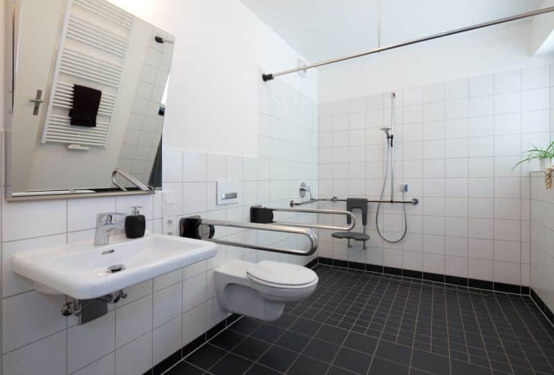Bad Barrierefrei Ein modernes barrierefreies Bad mit Stützhilfe an der Toilette, einem Sitz in der Dusche und bodentiefem Duschbereich.