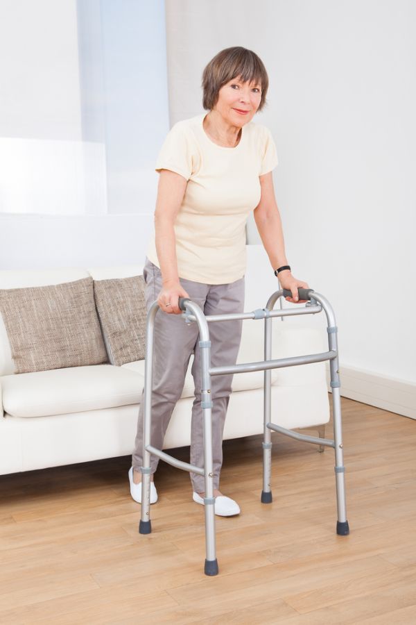 Gehhilfe Eine ältere Frau mit einer Gehhilfe steht von ihrem Sofa in ihrer Wohnung auf.