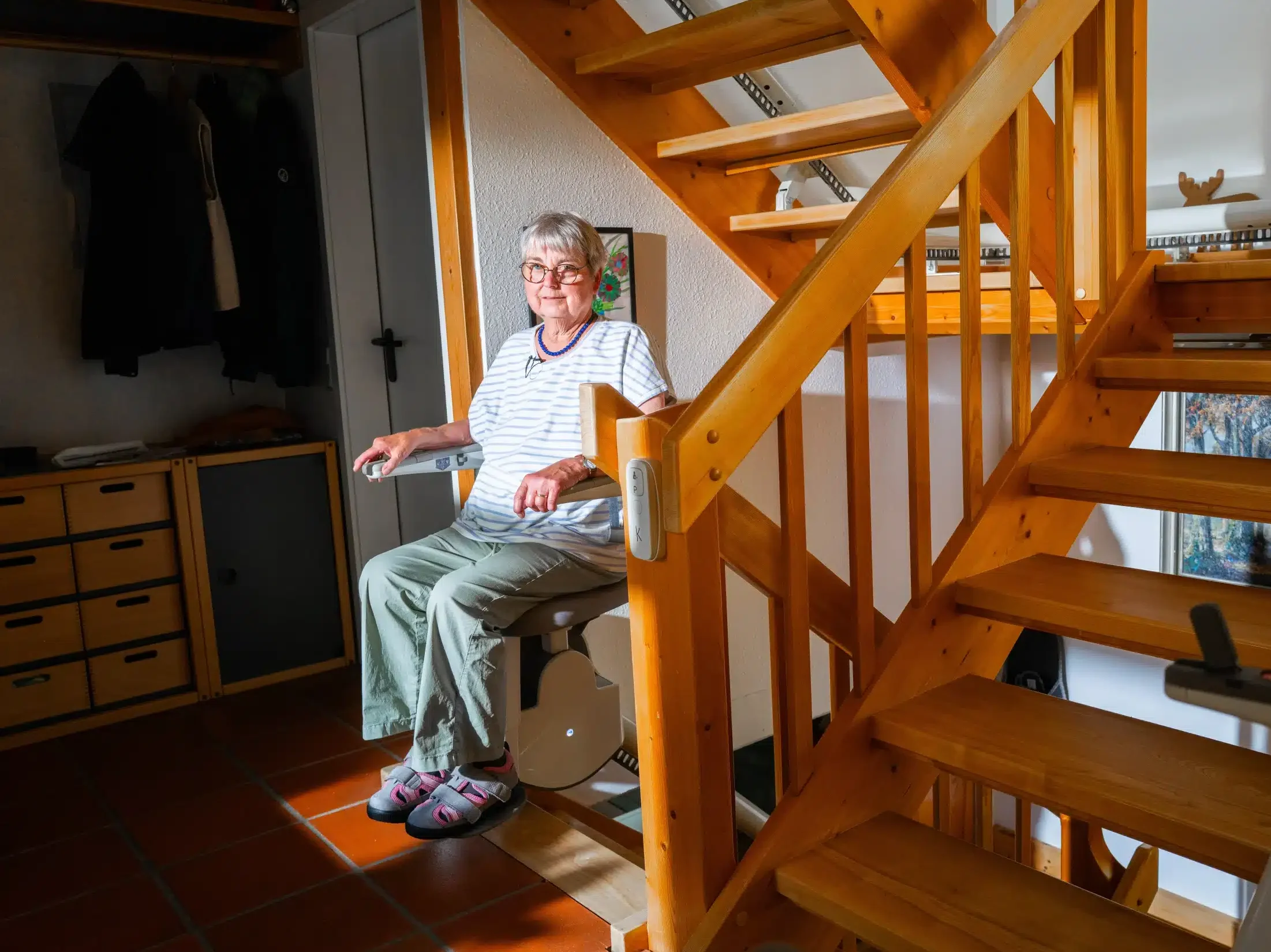 Kundin sitzt auf ihrem Treppenlift am Fuß einer Holztreppe